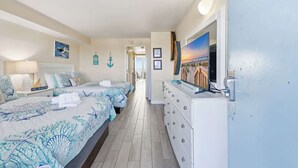 Ein Schlafzimmer mit zwei Betten, einem Schminktisch, einem Fernseher und Blick auf den Strand.