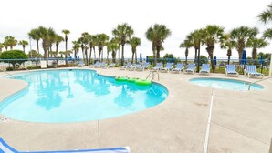 Ein Poolbereich mit zwei Pools, Liegestühlen und Palmen.