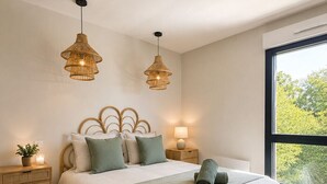 Un dormitorio moderno con una cama grande, dos mesitas de noche, una lámpara de noche, un ventanal con vistas y dos lámparas colgantes.