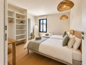 A bedroom with two beds, a wooden table, a wardrobe, and a large window. - Villa 29 – pool – golf – nature – 6/8 people (Talmont-Saint-Hilaire)