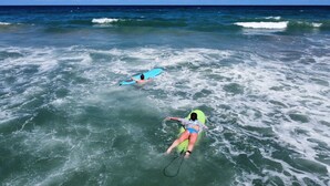 Zwei Personen surfen im Meer bei Wellen.