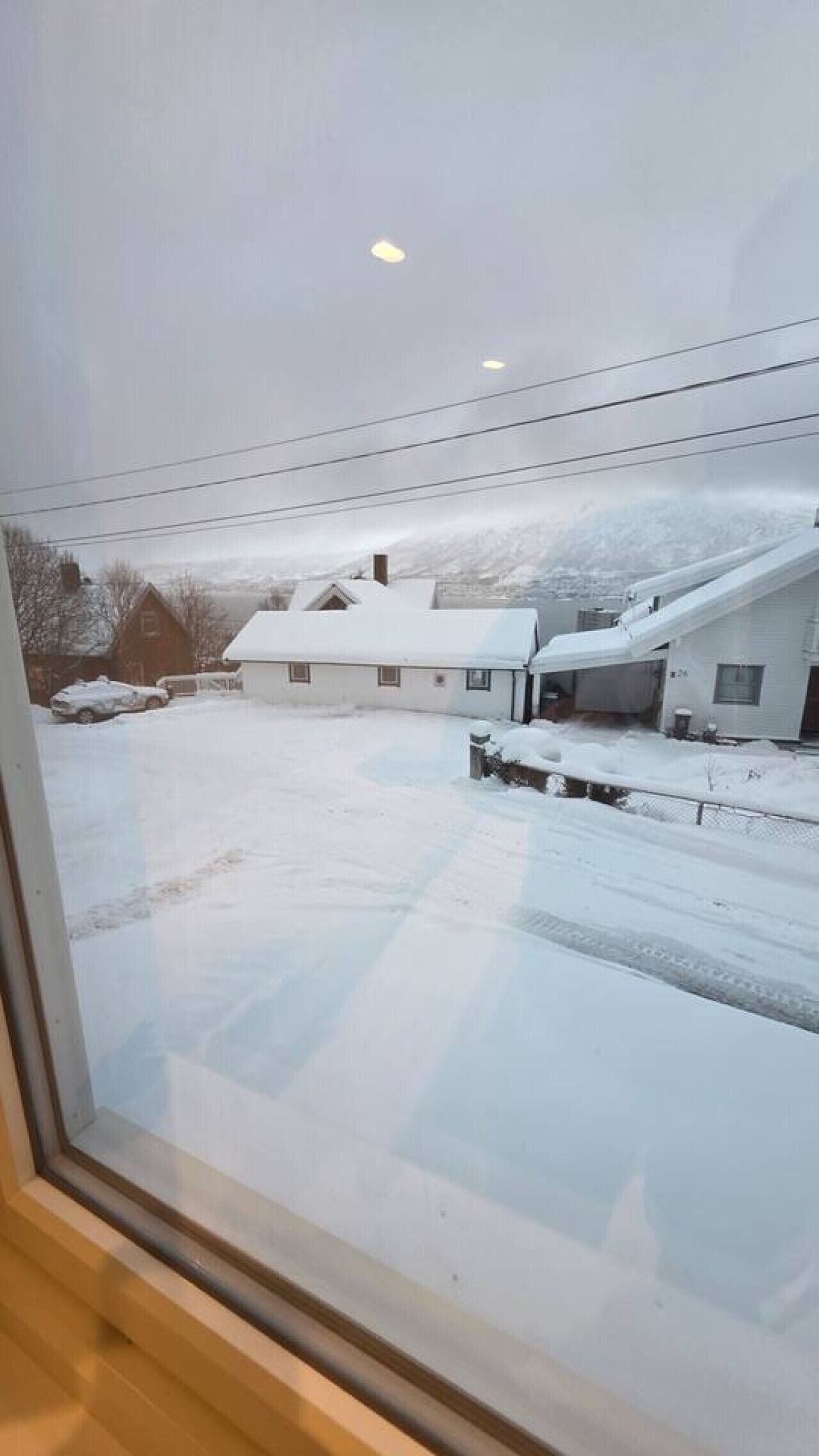 A view of a residential area with houses covered in snow, a clear sky, and visible power lines.