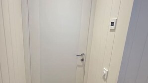 Un pasillo estrecho con una puerta de vidrio esmerilado, un interruptor de luz y un termostato en la pared.