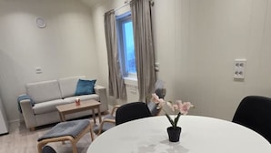 Un salon moderne avec une table de salle à manger ronde, des chaises noires, un canapé et une fenêtre avec des rideaux.