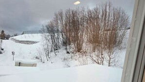 Paisaje nevado con árboles desnudos y un edificio al fondo.