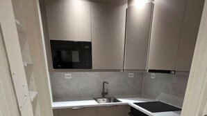 Una cocina compacta con horno integrado, un lavamanos y un microondas.