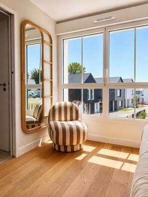 A bedroom with a large window, a striped armchair, and a mirror. - Villa 18 – pool – golf – nature – 6/8 people (Talmont-Saint-Hilaire)