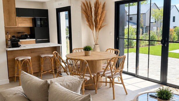 Une cuisine moderne avec des meubles noirs, un coin repas avec des chaises en osier et une grande porte-fenêtre coulissante donnant sur une terrasse.