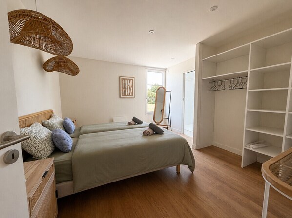 Un dormitorio con dos camas, un armario, un espejo y una silla colgante.
