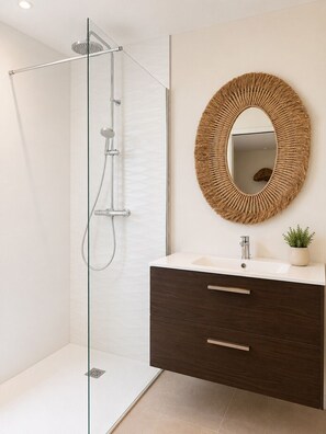 A modern bathroom with a glass-enclosed shower, a round mirror, and a dark wood vanity with a white sink.