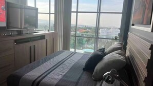 Une chambre avec un grand lit, une télévision et une vue sur le paysage urbain, grâce à de grandes fenêtres.