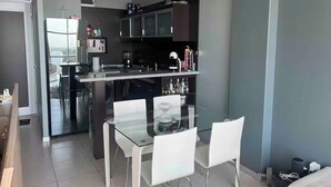 Une cuisine moderne avec une table à manger en verre et des chaises blanches, un four encastré et un réfrigérateur.