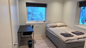 Une petite pièce bien éclairée, avec un lit, un bureau et une fenêtre.