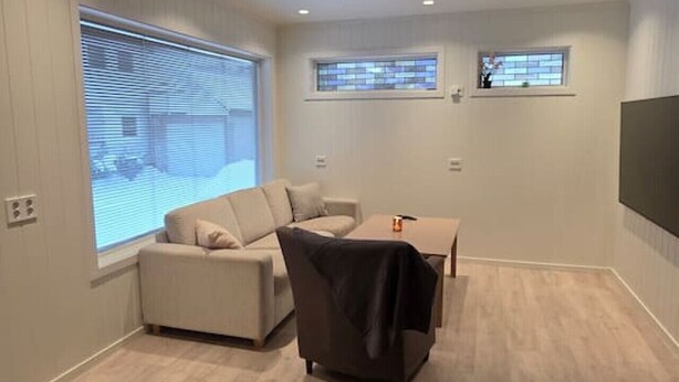Een moderne woonkamer met een groot raam, een bank, een salontafel en een flatscreen televisie aan de muur.