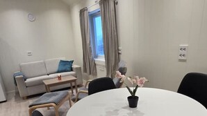 Een moderne woonkamer met een ronde eettafel, zwarte stoelen, een bank en een raam met gordijnen.