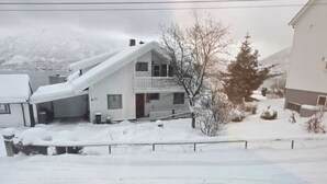 Een woonwijk met een huis met twee verdiepingen, bedekt met sneeuw, een geparkeerde auto en een heldere lucht.