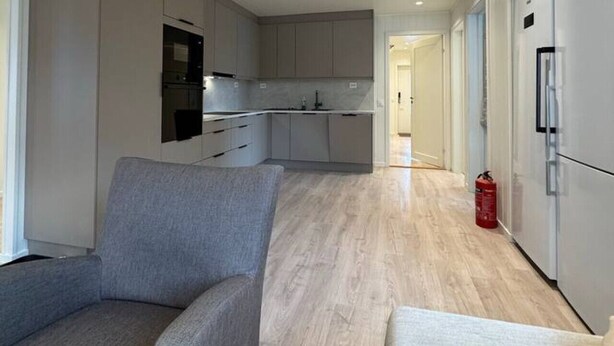 Een moderne keuken met grijze kastjes, een ingebouwde oven en een magnetron. In de woonkamer staan twee grijze banken en een klein tafeltje.