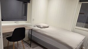 Een kleine slaapkamer met een bed, bureau en stoel.