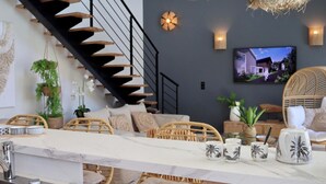 A modern kitchen with a marble countertop, wooden staircase, wicker furniture, and a TV mounted on the wall. - Villa 10 – pool – golf – nature – 6/8 people (Talmont-Saint-Hilaire)
