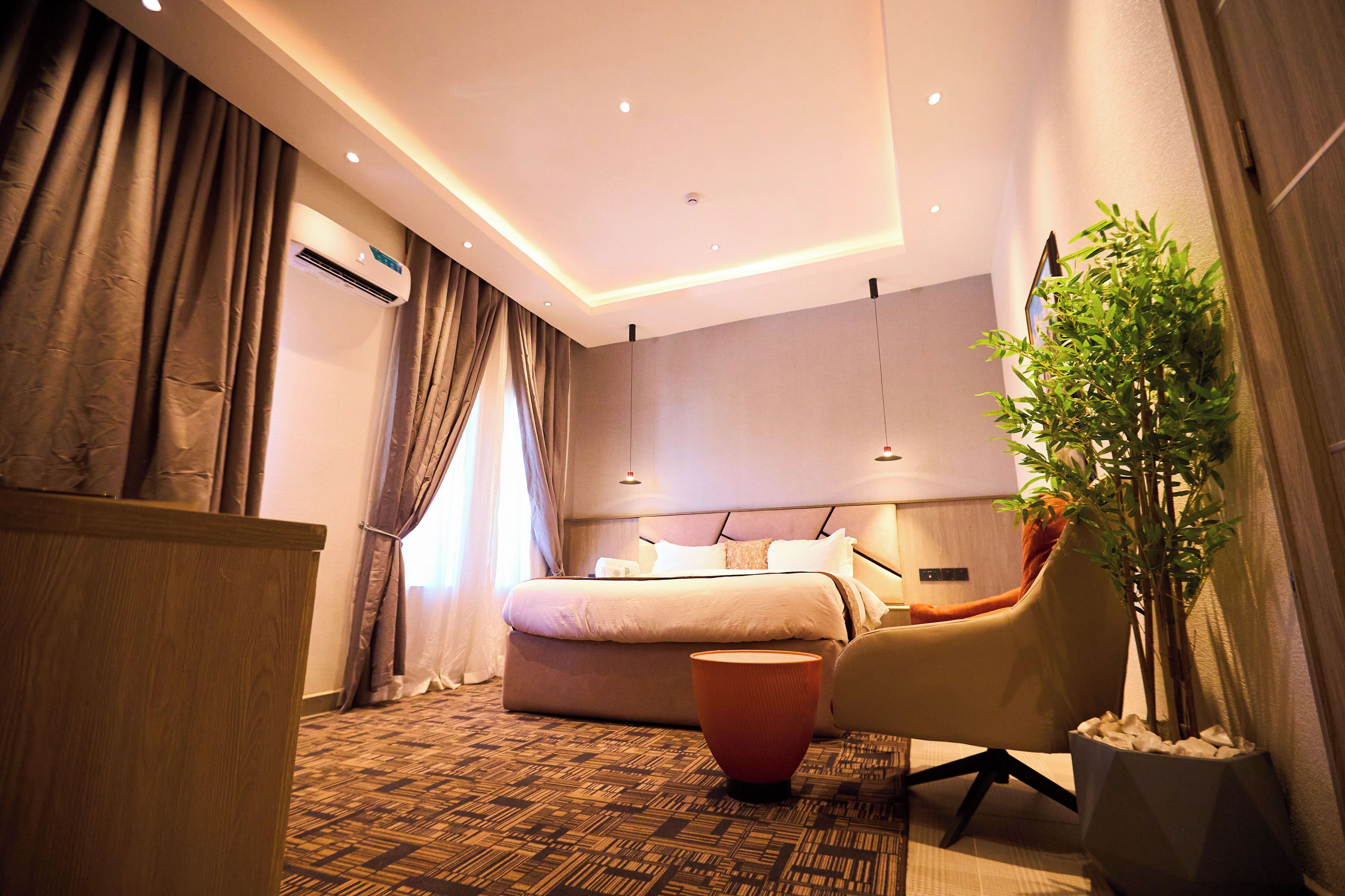 Ein modernes Hotelzimmer mit einem großen Bett, einer Sitzecke mit Sessel und Tisch, einer Klimaanlage und einer Zimmerpflanze.