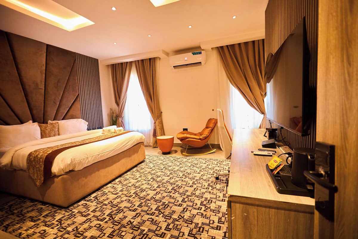 Een hotelkamer met een groot bed, een zithoek met een fauteuil, een flatscreen televisie en een airconditioningsapparaat.