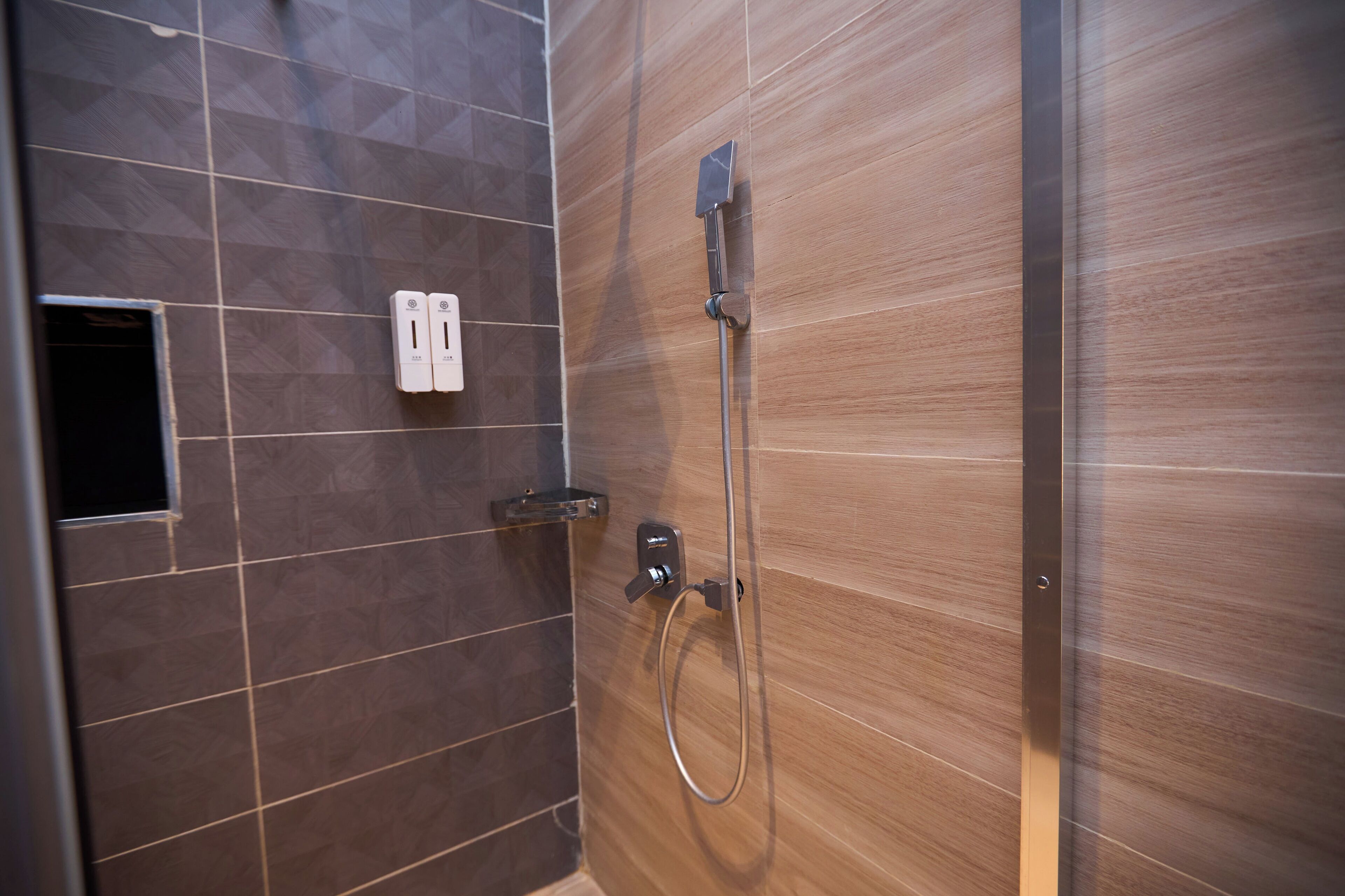 A shower with a handheld showerhead and a wall-mounted control panel.