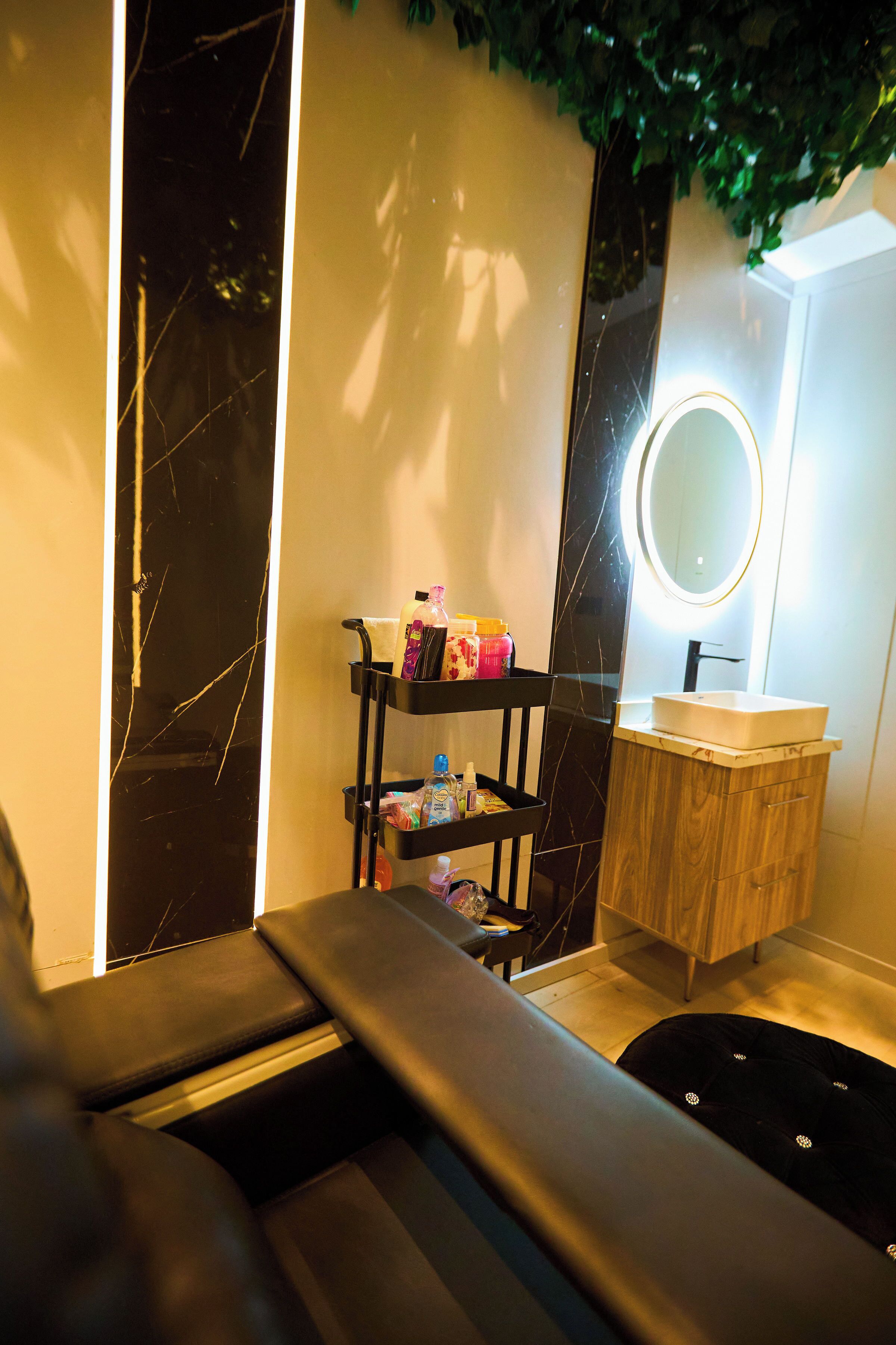 Une salle de bain moderne avec un meuble-lavabo en marbre noir, un miroir rond et une étagère contenant des articles de toilette.