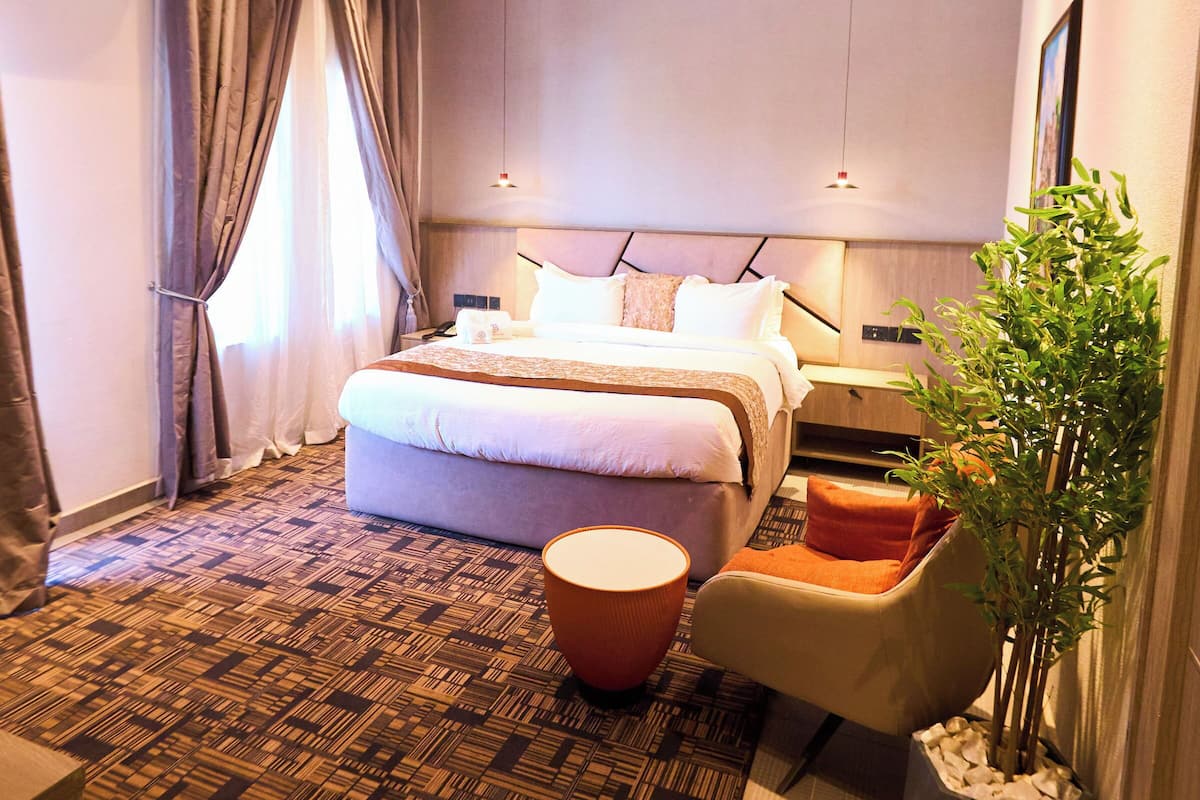 Een moderne hotelkamer met een groot bed, een klein zithoekje, een potplant en een luchtverkoeleenheid in het plafond.