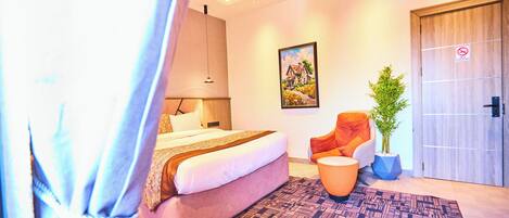 A modern hotel room with a bed, a chair, a potted plant, and a painting on the wall.
