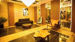 Eine moderne Lobby mit einer schwarzen Couch, einem Holztisch, einem Hängekorbstuhl und einem geometrischen Wanddesign.