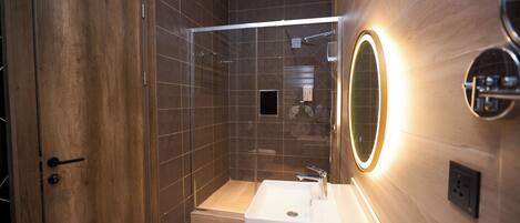 Une salle de bain moderne avec une douche à l’italienne en verre, un lavabo blanc et un miroir doté d’un cadre éclairé.