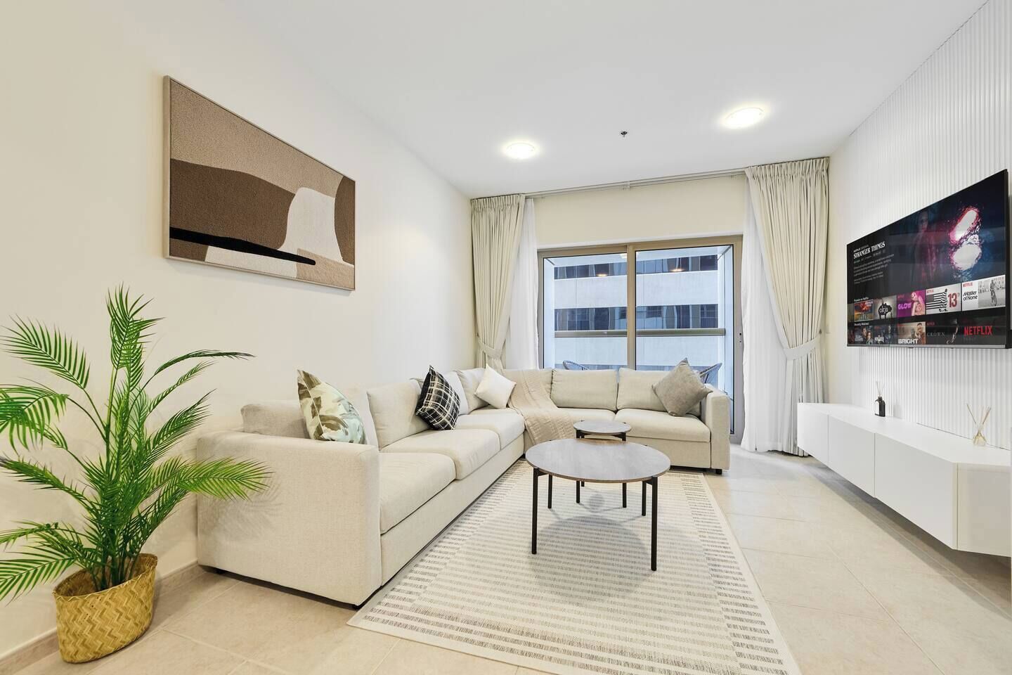 Een moderne woonkamer met een beige bank, een salontafel en een groot raam met gordijnen.
