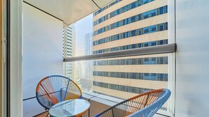Varanda com duas cadeiras e uma mesa pequena, com vista para um horizonte urbano com edifícios altos.