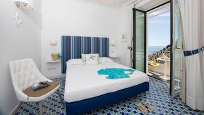 Habitación de hotel con una cama, una silla, una mesita de noche, una lámpara y vista al mar.