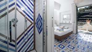 Un baño moderno con ducha, cama con vistas y balcón con mesa y sillas.