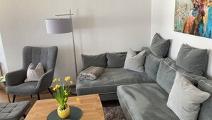 A modern living room with a grey sofa, a grey armchair, a wooden coffee table with a vase of yellow flowers, and a floor lamp. - Country life, quiet and modern on our farm, bay window apartment with great views (Windeck)