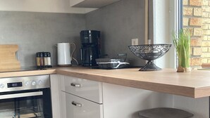 A kitchen with a built-in oven, a coffee maker, a kettle, and a small island with stools. - Country life, quiet and modern on our farm, bay window apartment with great views (Windeck)