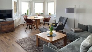 A modern living room with a wooden dining table, comfortable seating, a flat-screen TV, and a large window providing natural light. - Country life, quiet and modern on our farm, bay window apartment with great views (Windeck)