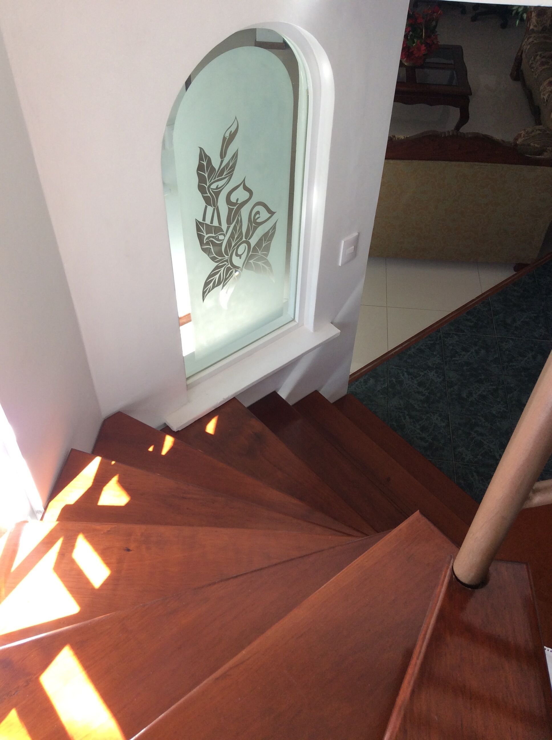 A wooden staircase with a frosted glass window featuring a decorative leaf pattern.