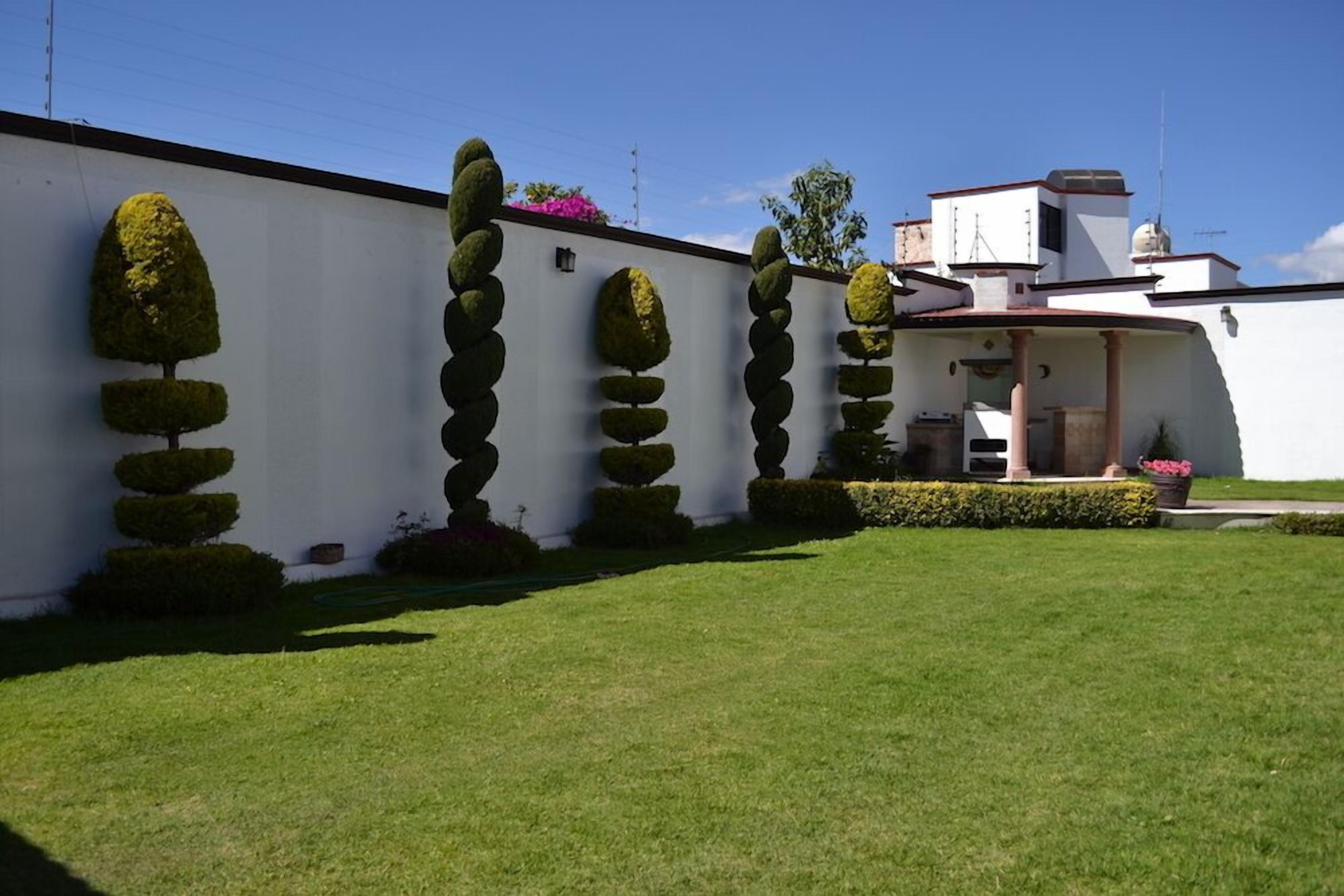 Un bâtiment blanc doté d’un jardin symétrique, agrémenté d’arbres taillés en formes géométriques et d’une pelouse bien entretenue.