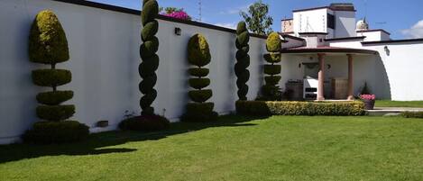 Un bâtiment blanc doté d’un jardin symétrique, agrémenté d’arbres taillés en formes géométriques et d’une pelouse bien entretenue.