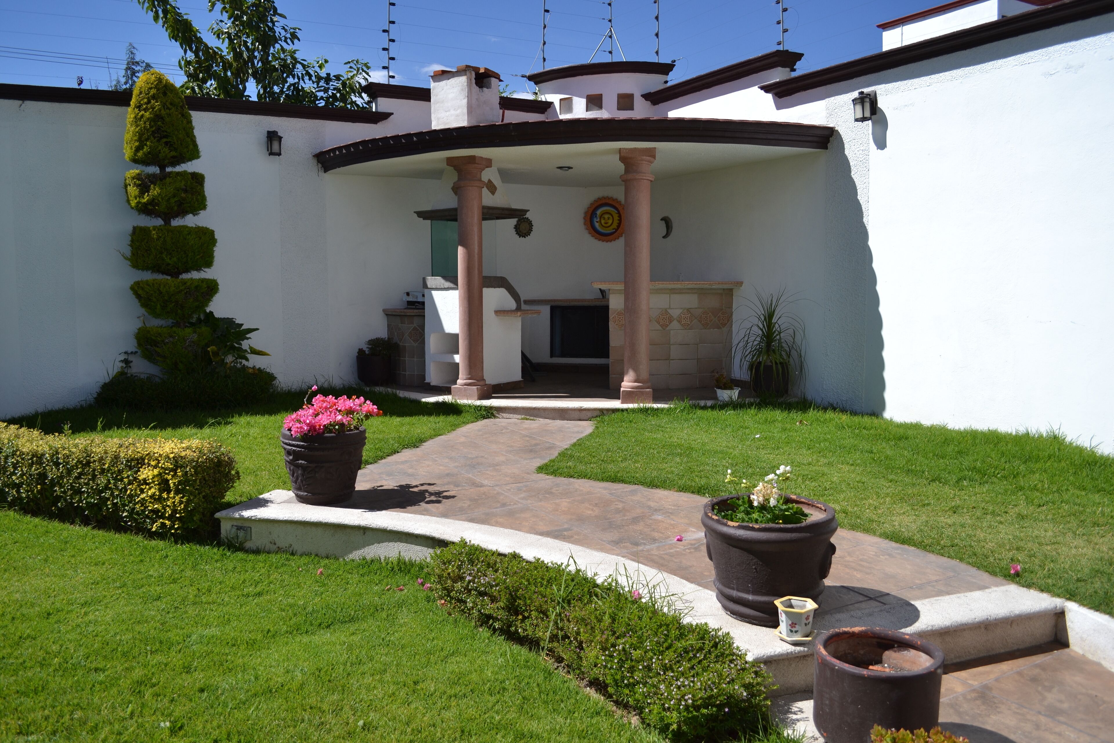 Un patio con una zona de estar cubierta, un sendero y plantas en macetas.
