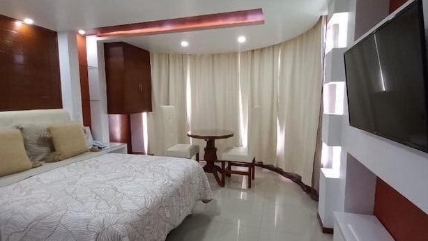 A modern hotel room with a large bed, a TV, a dining table with chairs, and a ceiling light fixture. - Hotel La Aurora (Huamantla)