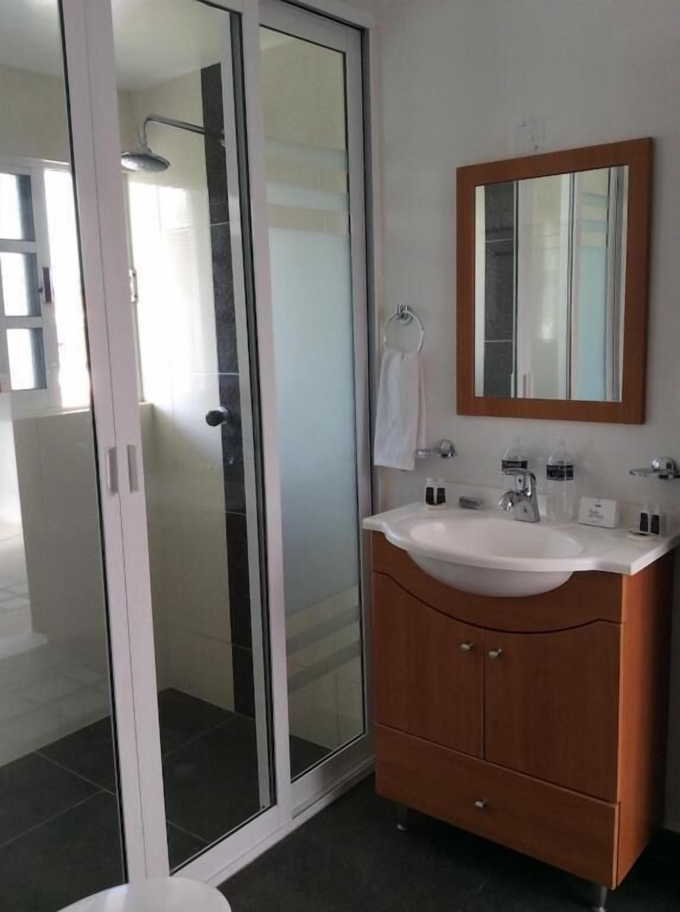 A modern bathroom with a glass shower enclosure, a wooden vanity with a sink, and a mirror.