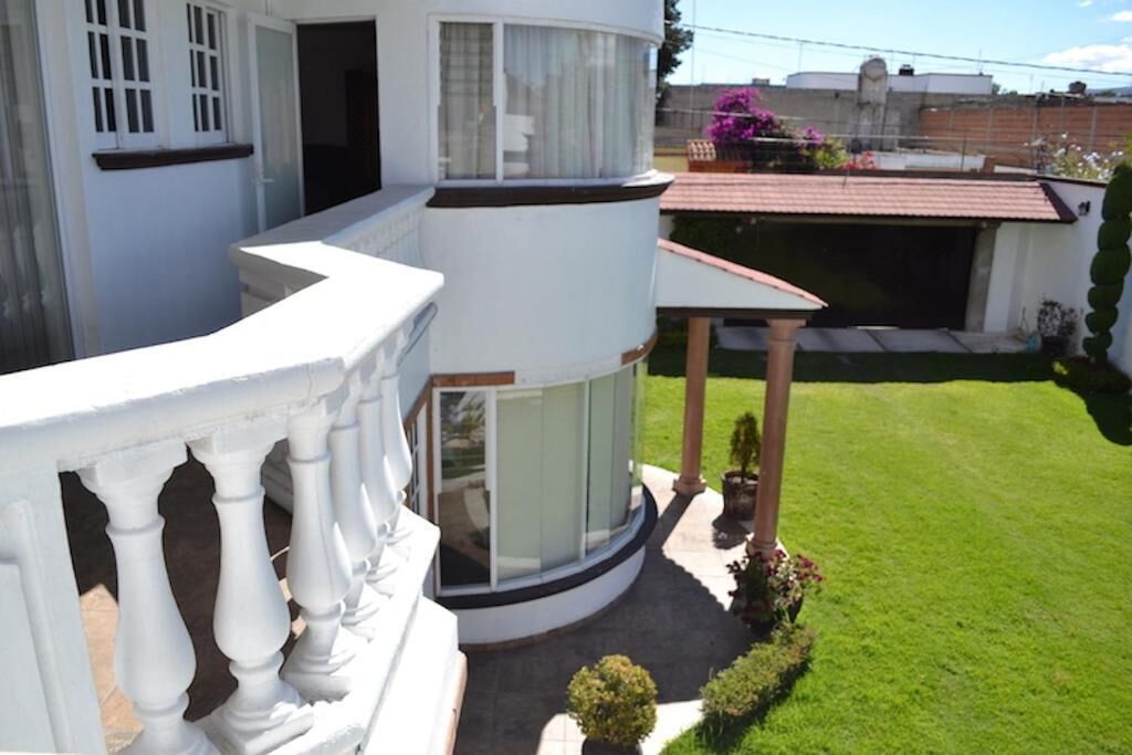 Un edificio blanco con un balcón, un área exterior techada y un césped bien cuidado.