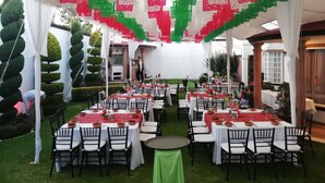 An outdoor dining area with tables set for guests, surrounded by neatly trimmed hedges and a white tent structure. - Hotel La Aurora (Huamantla)