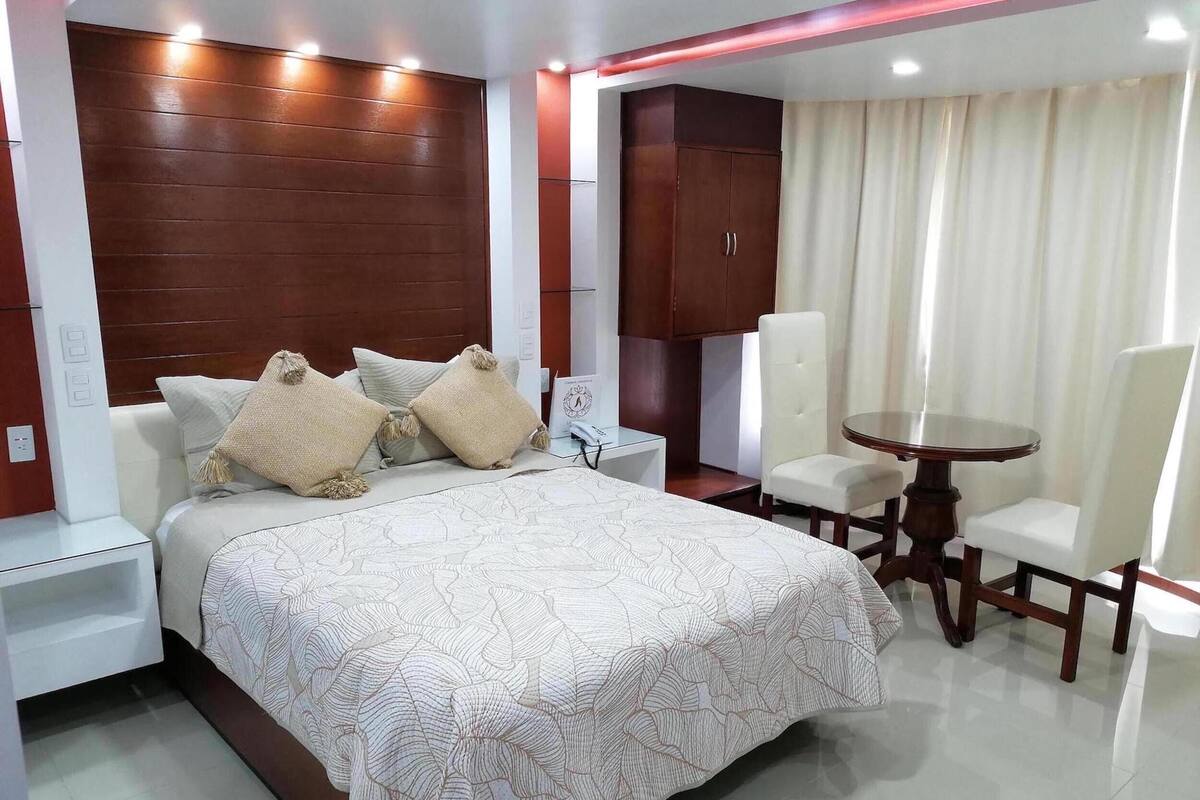 Habitación de hotel con una cama grande, cabecera de madera, una mesita con sillas y un armario.