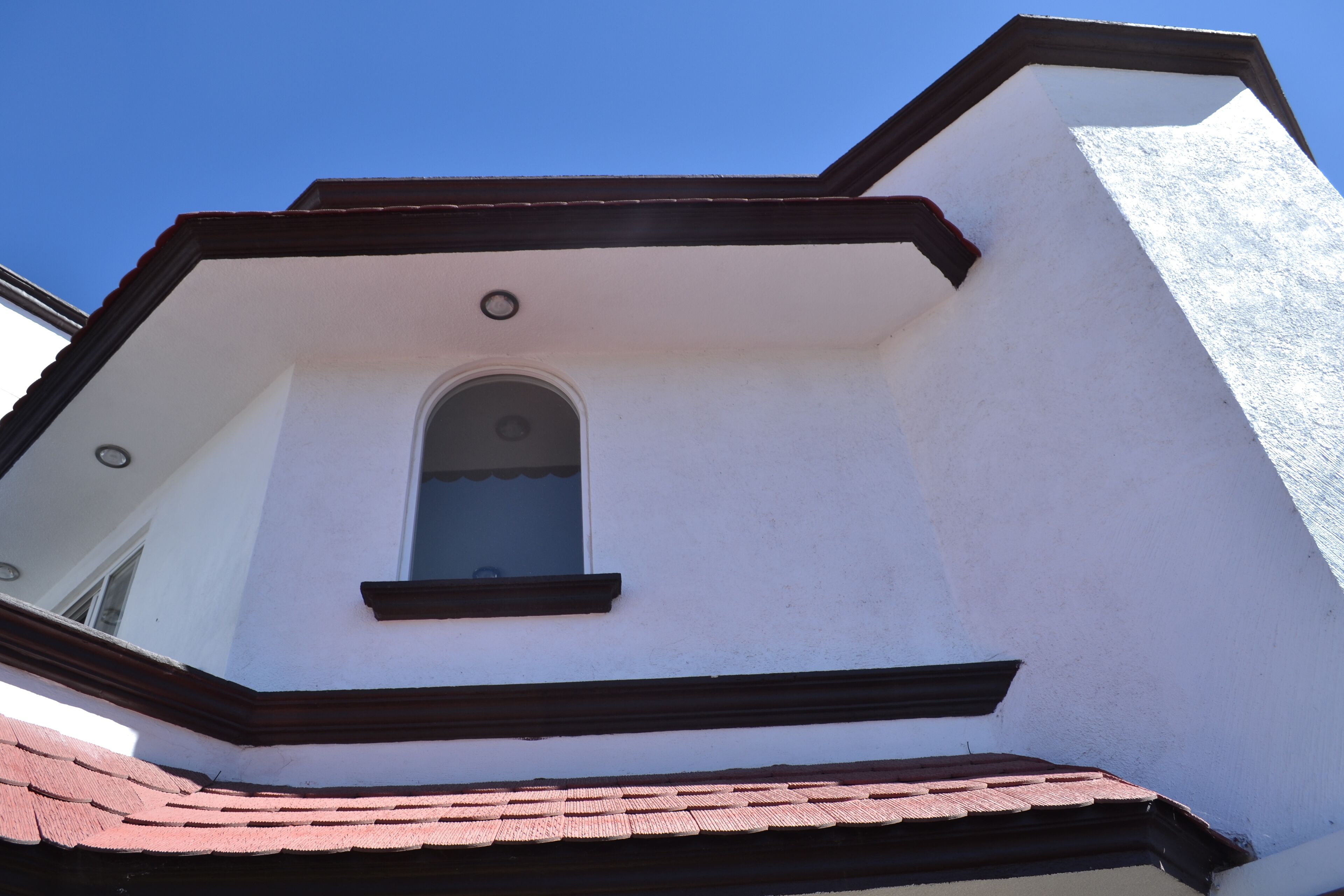 Una esquina de un edificio con fachada blanca, una ventana de marco oscuro y un tejado de tejas rojas.