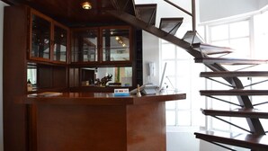 A wooden reception desk with a glass display case, a staircase with metal railings, and a view of the interior space. - Hotel La Aurora (Huamantla)