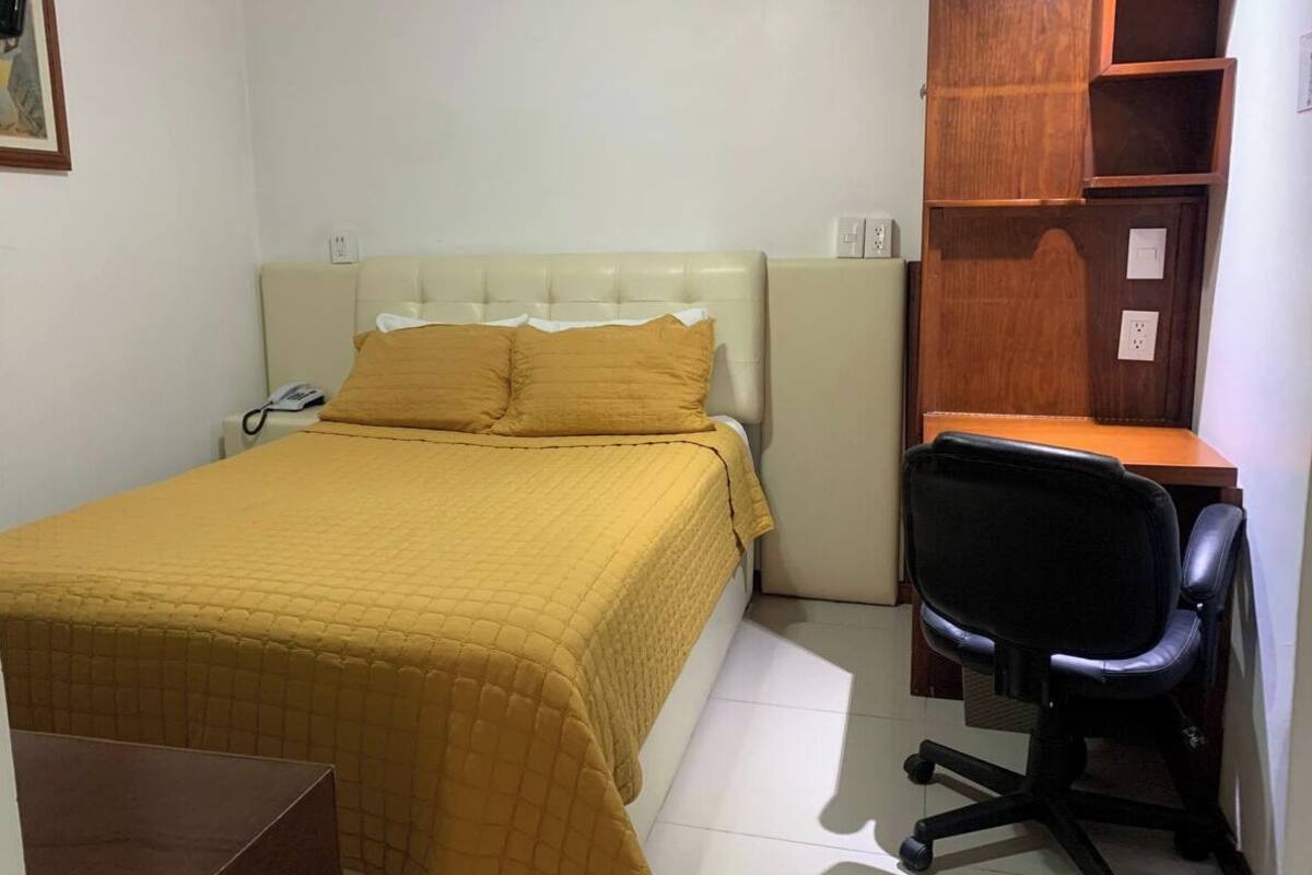 Un dormitorio pequeño y ordenado con cama, escritorio y silla.